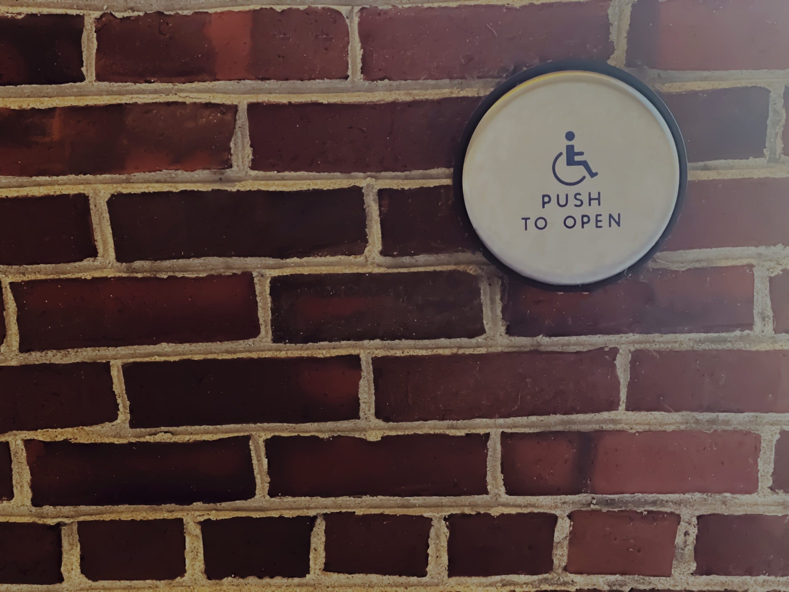 Image of a brick wall with a "push to open" ADA push button.