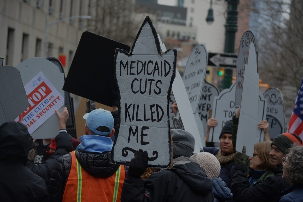 Demonstrators protest against Medicaid cuts, 2025. One sign in the shape of a tombstone reads "Medicaid cuts killed me."